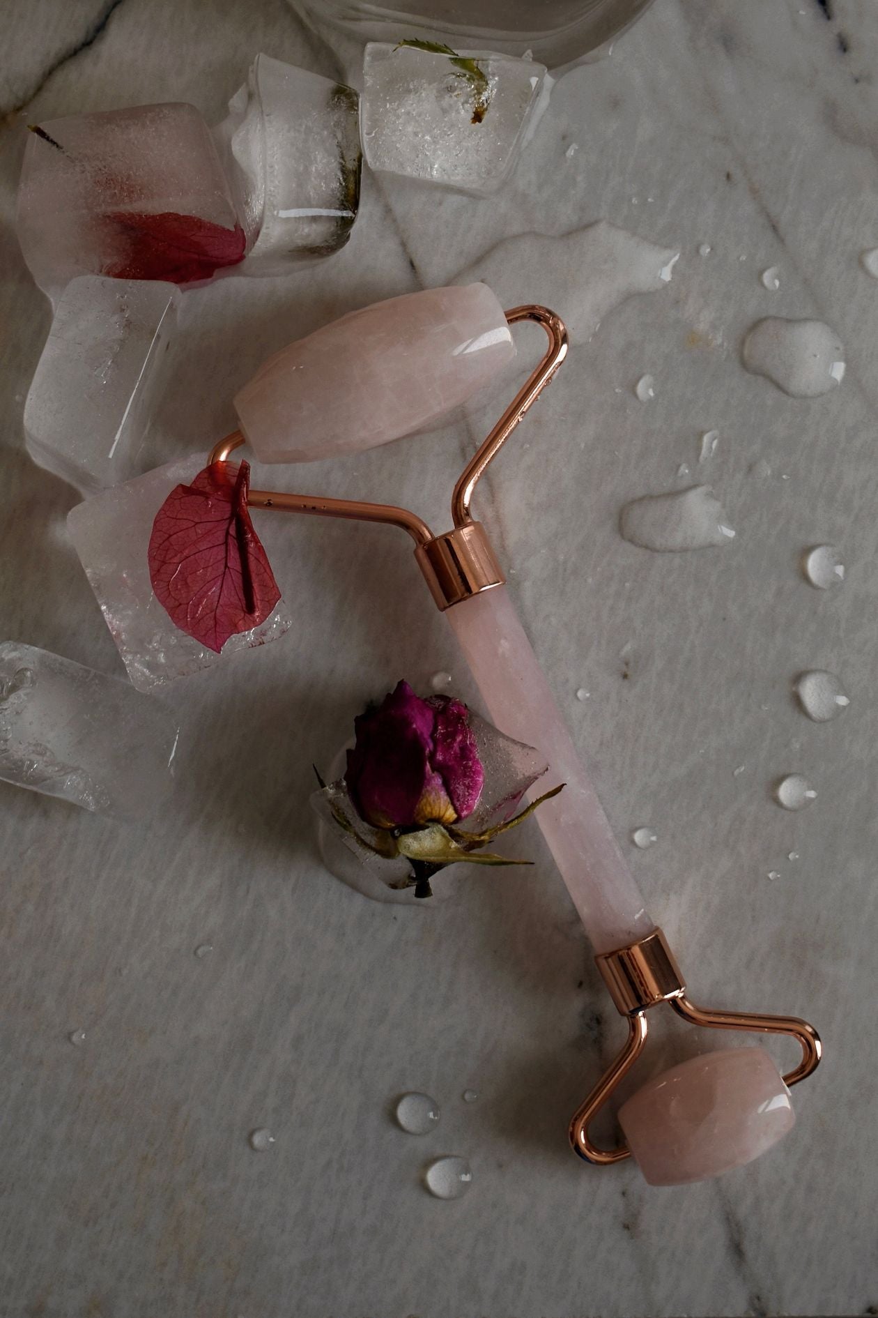 Rose quartz facial roller resting on ice cubes with flowers