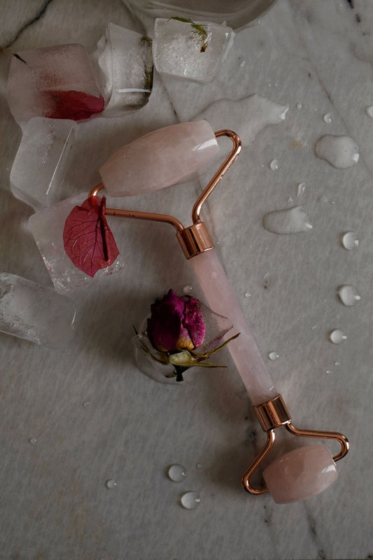 Rose quartz facial roller resting on ice cubes with flowers