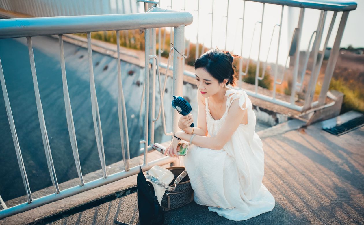 Woman using a handheld rechargeable fan outdoors in summer